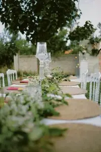 Beautifully decorated outdoor table with green foliage and glass candle holders, perfect for weddings.
